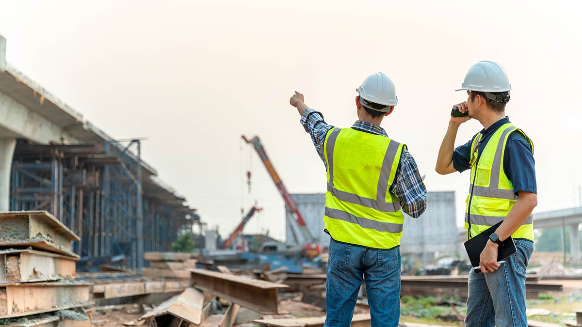 Due operai con casco e giubbotto ad alta visibilità osservano un cantiere edile